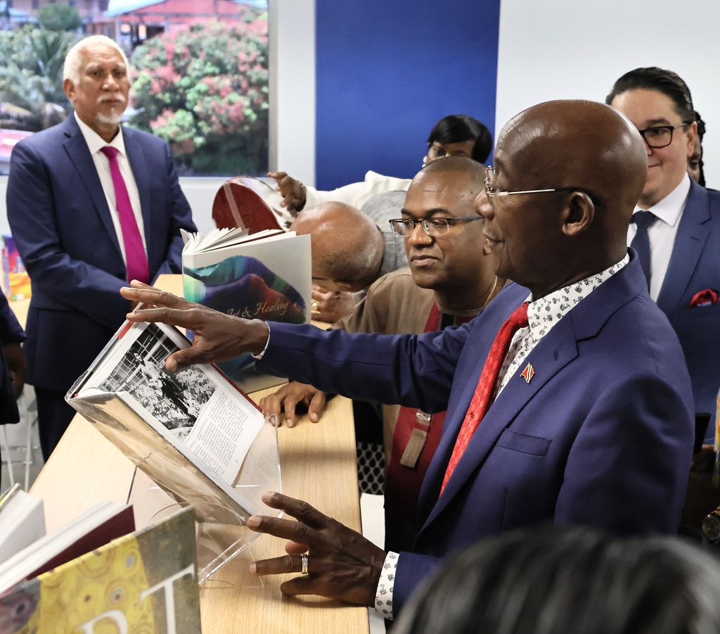 Prime Minister Dr Keith Rowley, right, and Nalis chairman Neil Parsanlal browse through a book titled, The Illustrated Story of Pan, written by former journalist Kim Johnson, during the official opening ceremony for the Diego Martin Public Library yesterday. Also in the photo from left are, Udecott chairman Noel Garcia, and Diego Martin Central MP Symon De Nobriga (partially hidden).