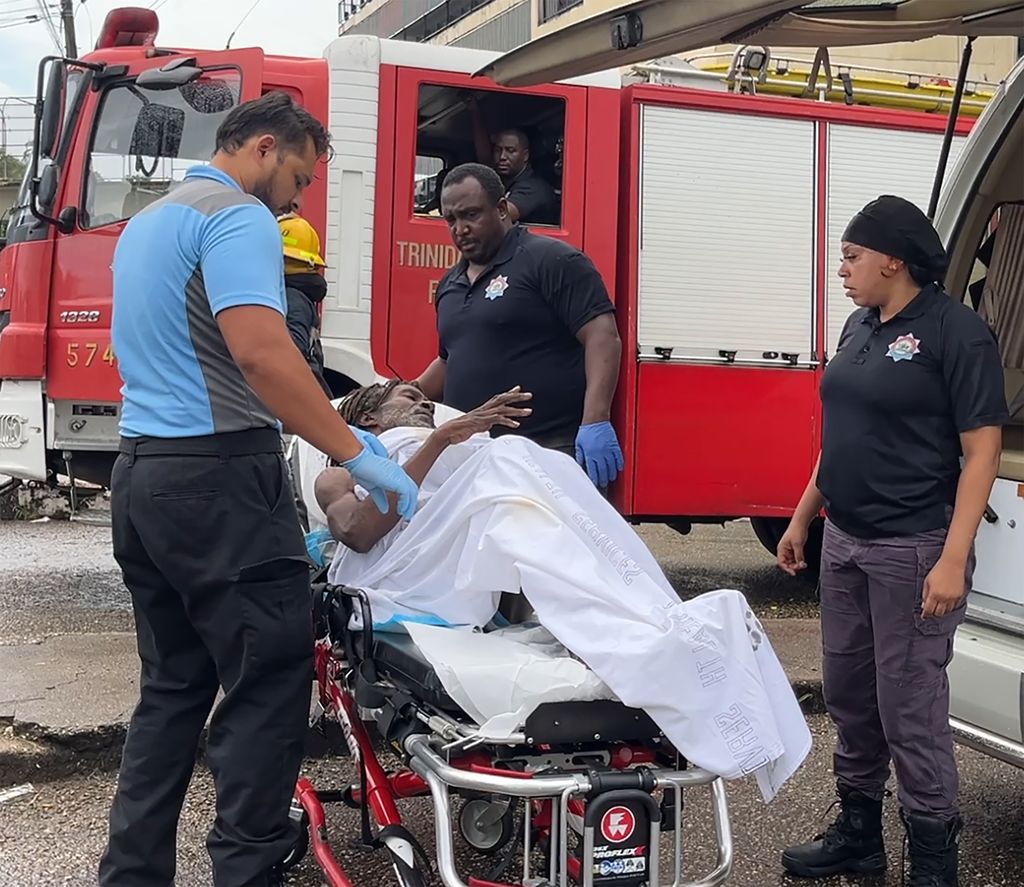 Fire Service officers and emergency personnel render medical assistance to Anderson Mark, who was rescued after clinging to a rope to avoid being swept away by floodwaters surging through the East Dry River in Port-of-Spain yesterday.
